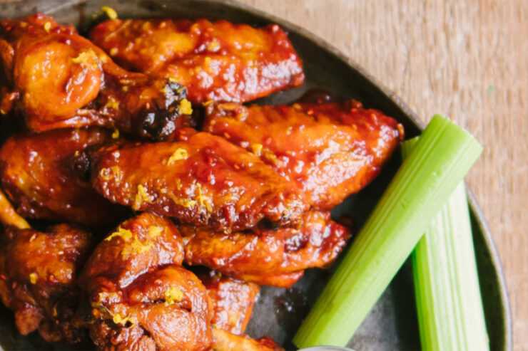 Black plate on wooden table with saucy wings and celery
