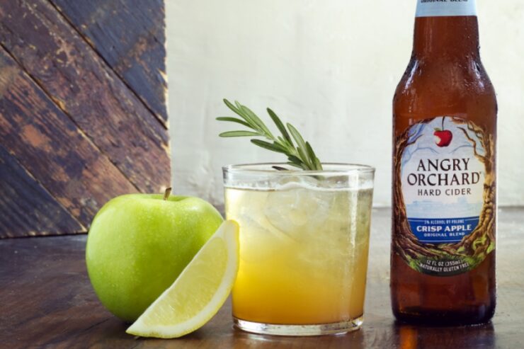 a cocktail, a green apple, a lemon wedge, and a bottle of angry orchard cider