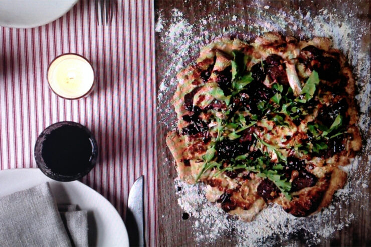 pizza pie on table with flour and balsamic vinegar on the left hand side on a striped table mat