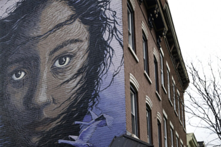 Mural on the side of a brown brick building of a girl with her hair blowing in the wind