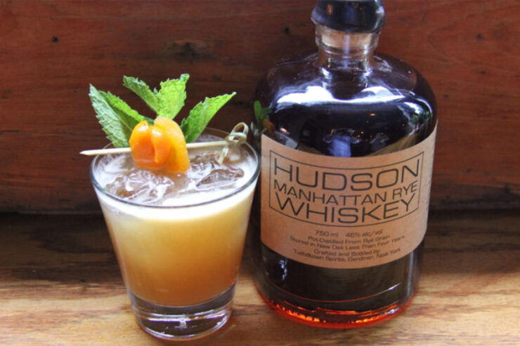 Birth of Aphrodite cocktail next to the Hudson Whiskey that was used in it on a wooden table