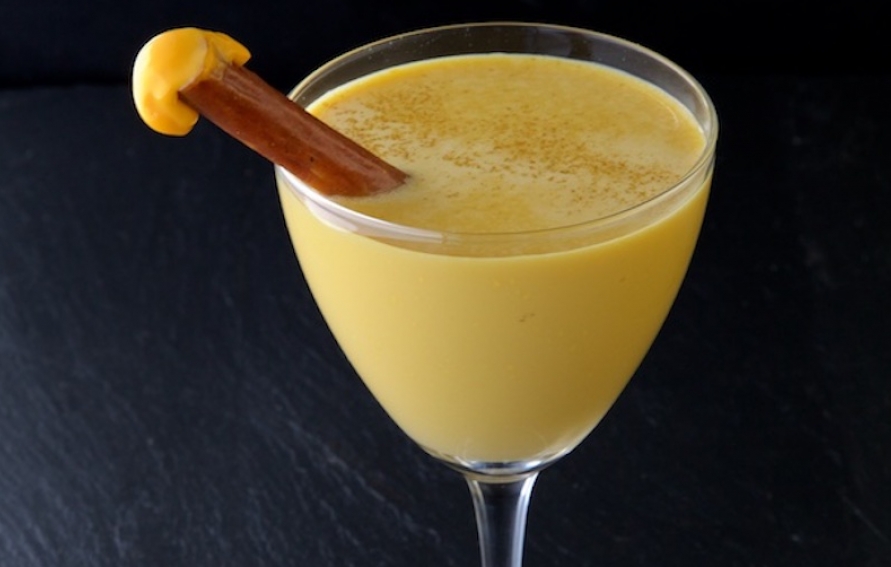 a yellow cocktail made with cheese with a pretzel garnish