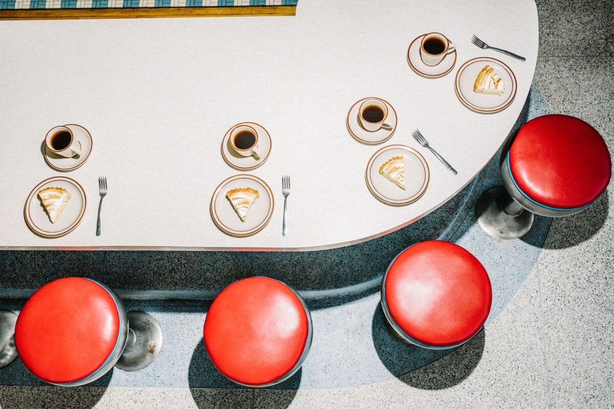 Retro dining table with four red seat bar stools and slices of pie and a cup of coffee in front of each stool